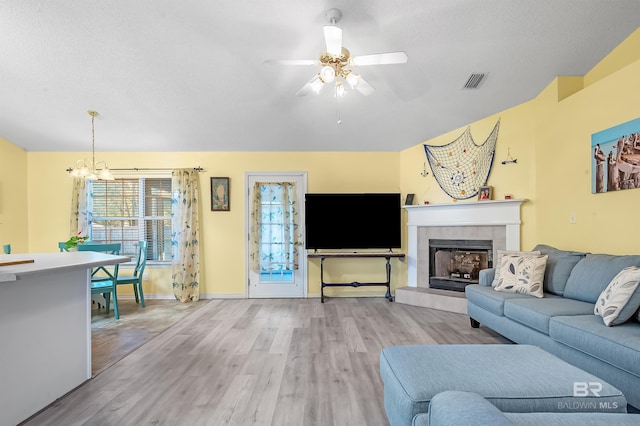 living room with a textured ceiling, a tiled fireplace, ceiling fan with notable chandelier, and light wood-type flooring