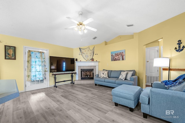 living room with light hardwood / wood-style floors, ceiling fan, lofted ceiling, and a tiled fireplace