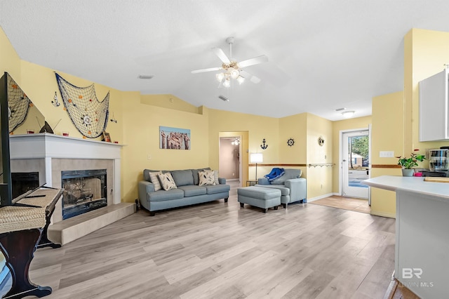 living room with light hardwood / wood-style flooring, ceiling fan, lofted ceiling, and a tiled fireplace