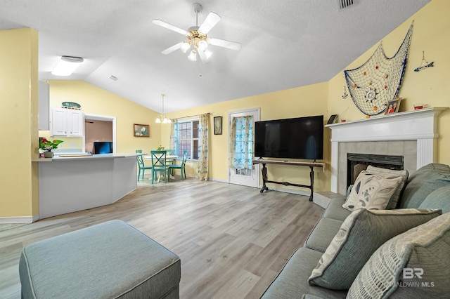 living room featuring ceiling fan with notable chandelier, vaulted ceiling, a fireplace, and light hardwood / wood-style flooring