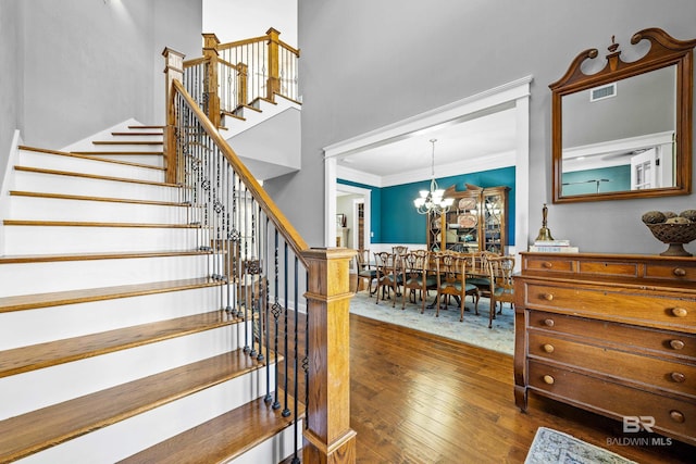 staircase featuring visible vents, a high ceiling, an inviting chandelier, ornamental molding, and wood finished floors