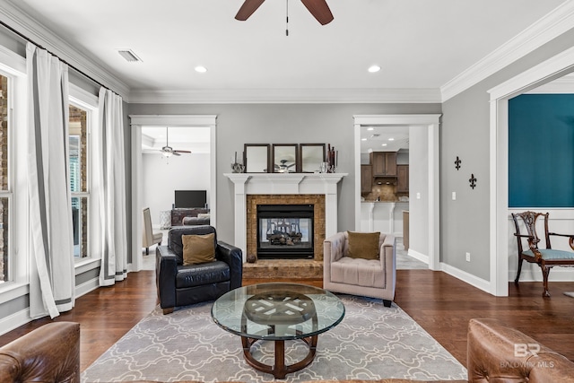 living area with dark wood-style floors, visible vents, crown molding, and a glass covered fireplace