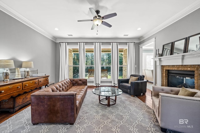 living room with ceiling fan, a glass covered fireplace, crown molding, and wood finished floors