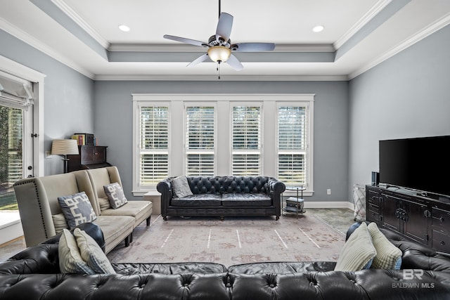 living area with ceiling fan, crown molding, a raised ceiling, and baseboards