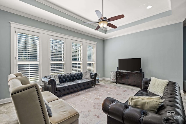 living room featuring ceiling fan, baseboards, ornamental molding, and a raised ceiling