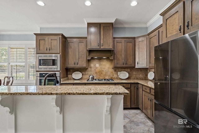 kitchen featuring light stone counters, decorative backsplash, appliances with stainless steel finishes, ornamental molding, and under cabinet range hood