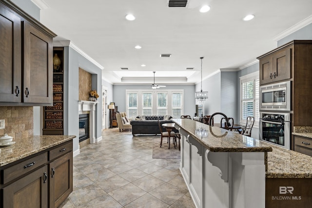 kitchen with a glass covered fireplace, a breakfast bar area, light stone counters, decorative light fixtures, and stainless steel appliances