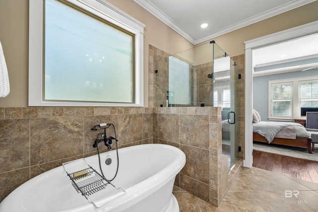 ensuite bathroom featuring tile walls, ornamental molding, a soaking tub, a shower stall, and ensuite bath