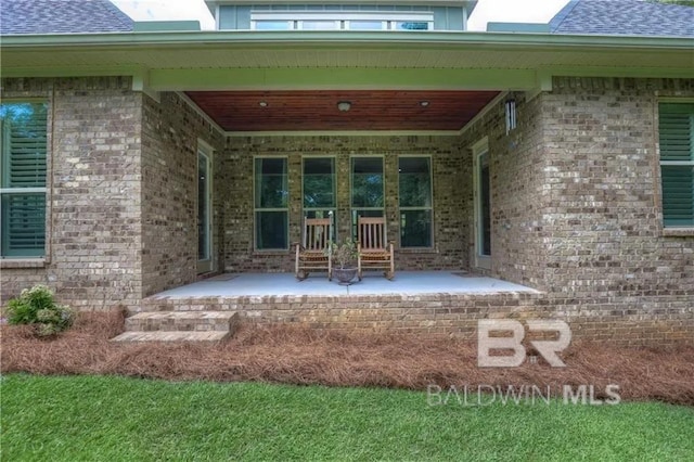 entrance to property with a patio area, brick siding, roof with shingles, and a porch