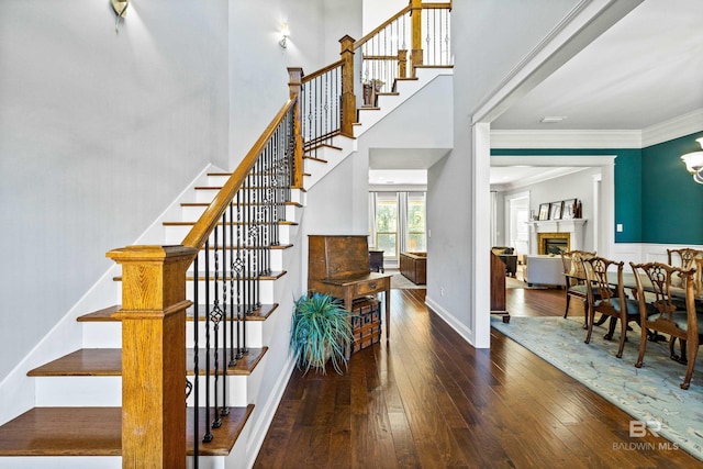 stairs with a fireplace, a towering ceiling, ornamental molding, wood finished floors, and baseboards