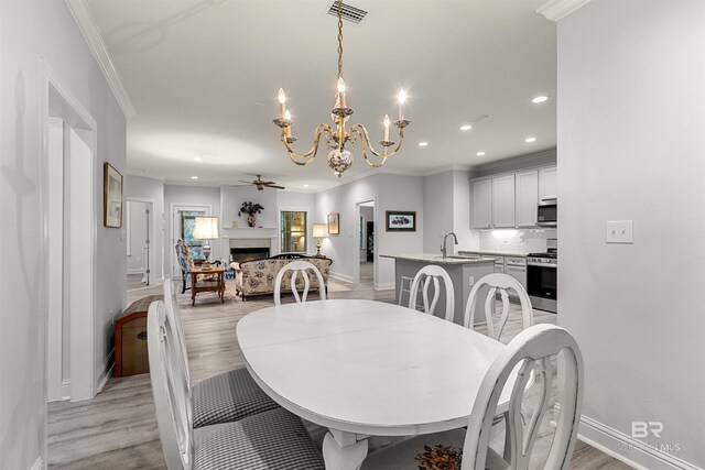 dining area with crown molding, ceiling fan with notable chandelier, light hardwood / wood-style flooring, and sink