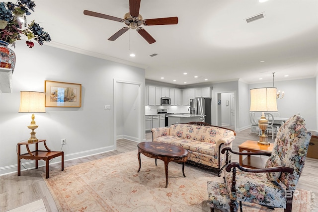 living room with ceiling fan with notable chandelier, crown molding, and light hardwood / wood-style flooring