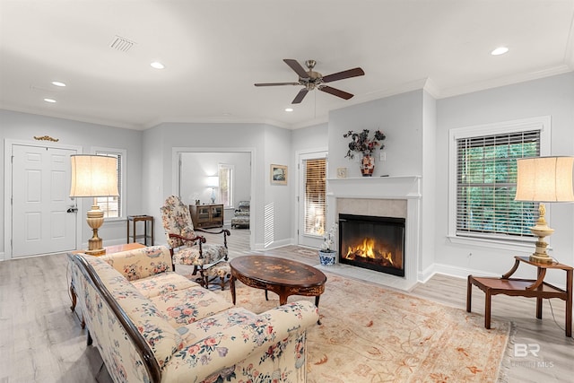 living room featuring ceiling fan, crown molding, light hardwood / wood-style floors, and a tiled fireplace