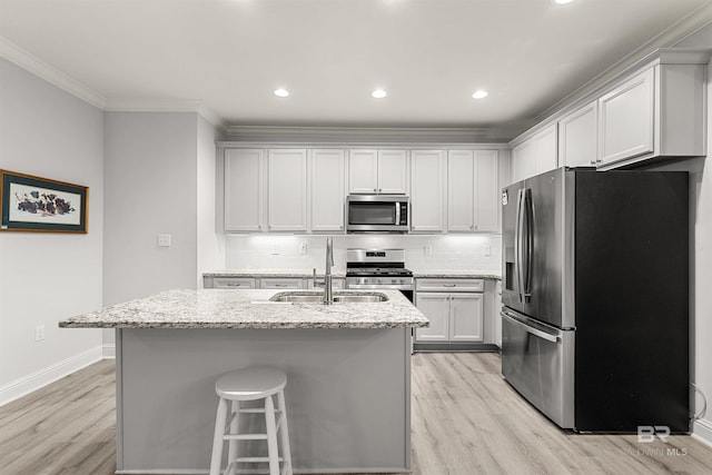 kitchen featuring a center island with sink, stainless steel appliances, white cabinets, light stone counters, and sink