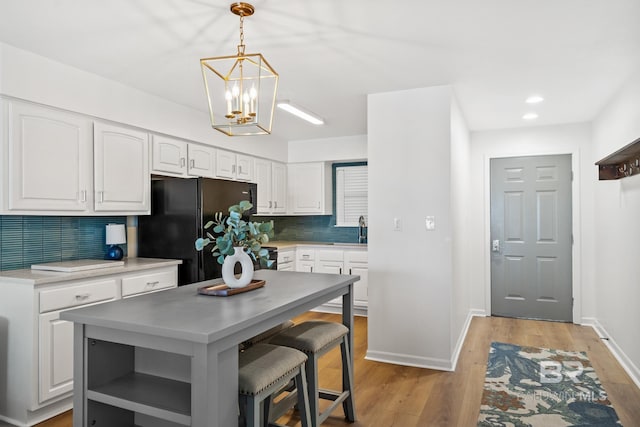 kitchen with white cabinetry, black refrigerator, decorative backsplash, a kitchen island, and pendant lighting