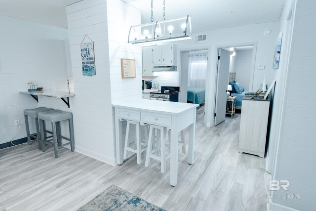 kitchen with a peninsula, a breakfast bar, white cabinetry, electric stove, and decorative light fixtures