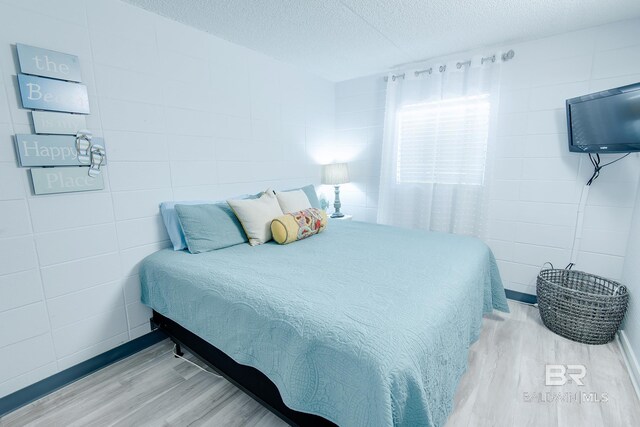 bedroom with light wood-type flooring, tile walls, and a textured ceiling