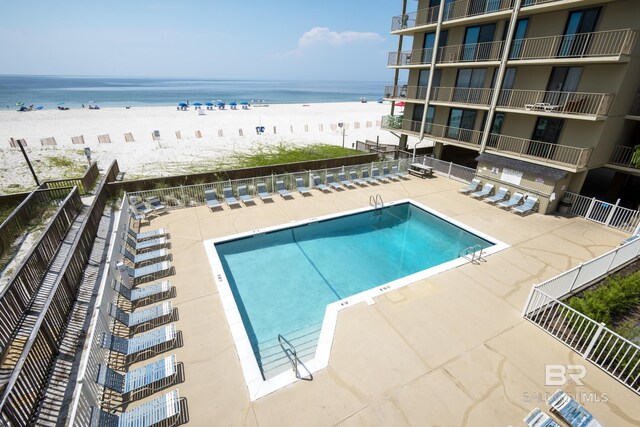 community pool with a patio, a water view, fence, and a view of the beach