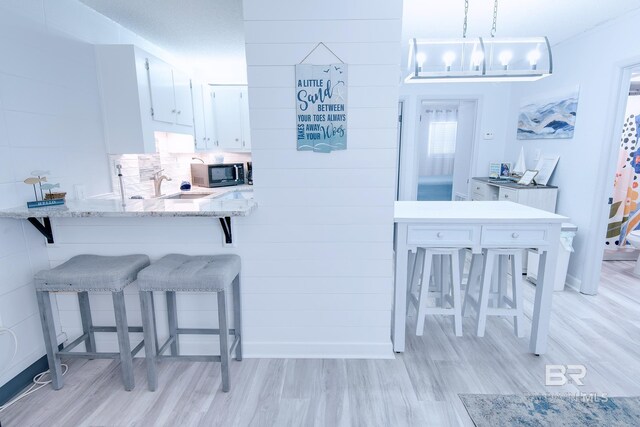 kitchen featuring a peninsula, a breakfast bar, white cabinetry, and pendant lighting