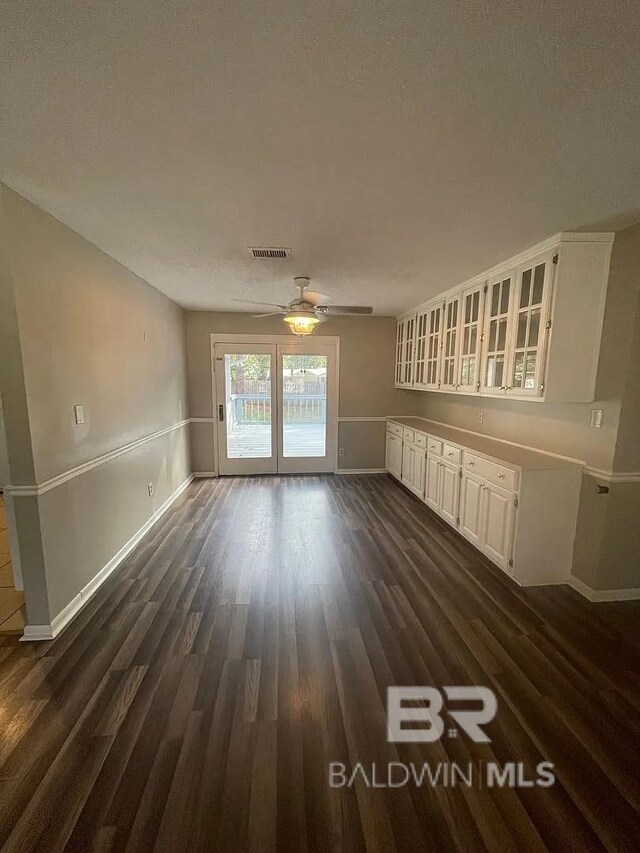 unfurnished dining area featuring ceiling fan, baseboards, and dark wood-style flooring