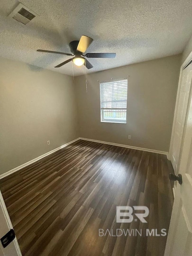 empty room with ceiling fan, baseboards, a textured ceiling, and dark wood-type flooring