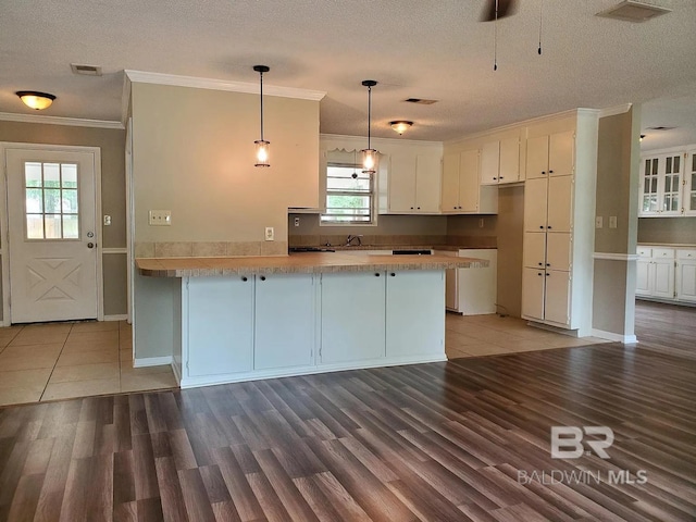kitchen with a peninsula, crown molding, a textured ceiling, white cabinetry, and light wood-type flooring