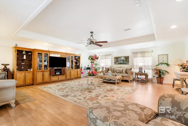 living room featuring ceiling fan, light hardwood / wood-style floors, and a tray ceiling