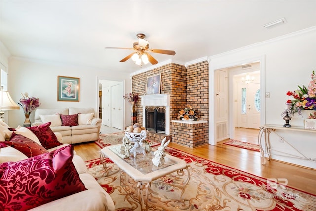 living room featuring crown molding, ceiling fan, light hardwood / wood-style floors, and a brick fireplace