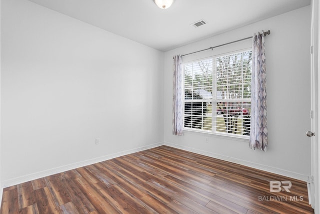 spare room featuring baseboards, visible vents, and wood finished floors