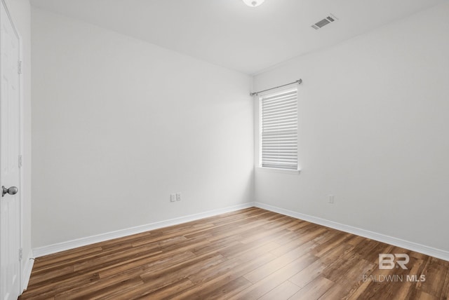 spare room with wood finished floors, visible vents, and baseboards