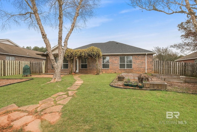 back of property featuring a yard, brick siding, a vegetable garden, and fence