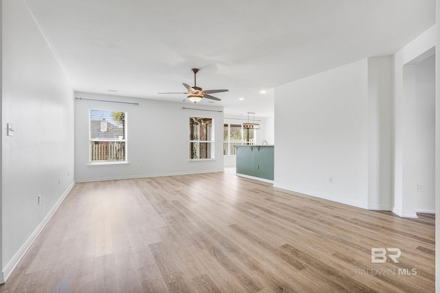 unfurnished living room with light wood finished floors, baseboards, and a ceiling fan