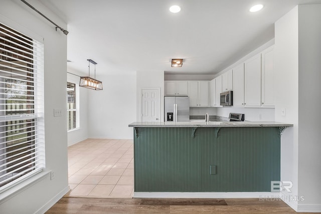 kitchen featuring stainless steel appliances, a peninsula, white cabinets, hanging light fixtures, and a kitchen bar