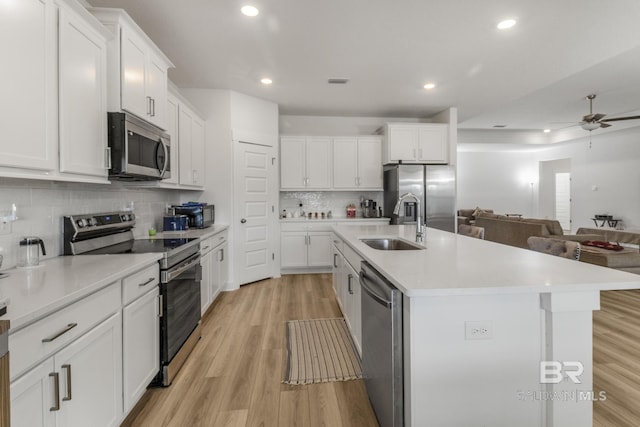 kitchen featuring light wood-style flooring, appliances with stainless steel finishes, white cabinets, a sink, and an island with sink