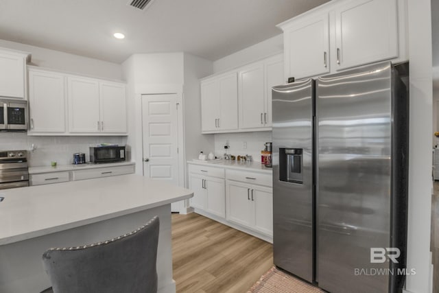 kitchen featuring backsplash, a breakfast bar, stainless steel appliances, light hardwood / wood-style flooring, and white cabinetry