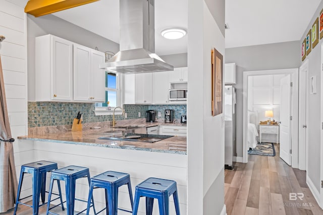 kitchen featuring a sink, light stone counters, backsplash, appliances with stainless steel finishes, and island range hood