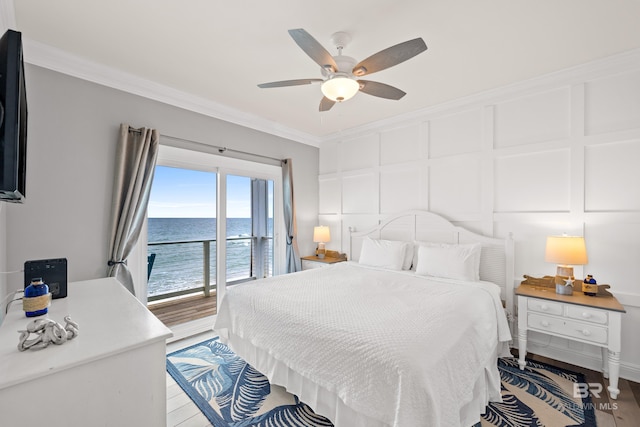 bedroom with a water view, access to outside, wood finished floors, crown molding, and a decorative wall