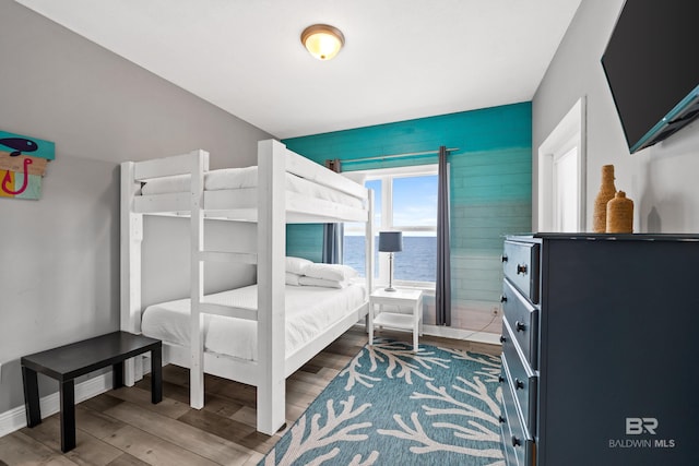 bedroom featuring wood finished floors, a water view, and baseboards