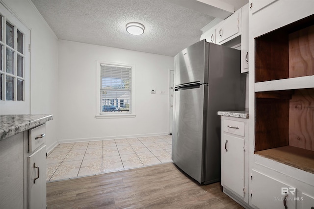 kitchen with stainless steel refrigerator, a textured ceiling, light wood-type flooring, and white cabinets