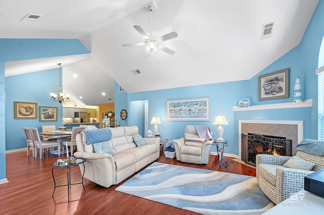 living room with ceiling fan with notable chandelier, dark hardwood / wood-style flooring, lofted ceiling, and a tile fireplace