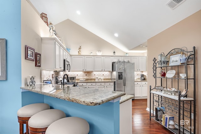 kitchen with white cabinets, light stone counters, lofted ceiling, and stainless steel appliances