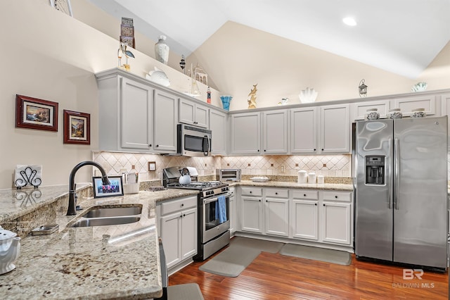 kitchen with light stone countertops, appliances with stainless steel finishes, sink, high vaulted ceiling, and white cabinets