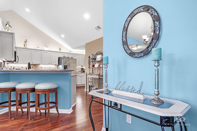 kitchen featuring light stone countertops, dark hardwood / wood-style flooring, stainless steel fridge, lofted ceiling, and decorative backsplash