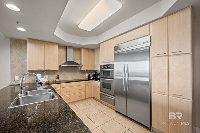 kitchen featuring wall chimney range hood, light brown cabinetry, appliances with stainless steel finishes, a warming drawer, and a sink