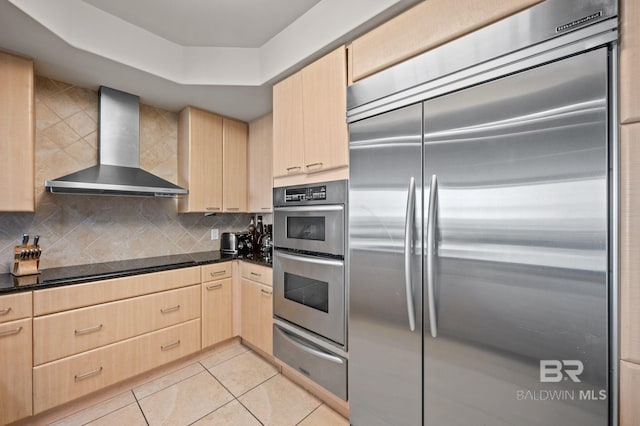 kitchen featuring light brown cabinets, wall chimney range hood, decorative backsplash, stainless steel appliances, and a warming drawer