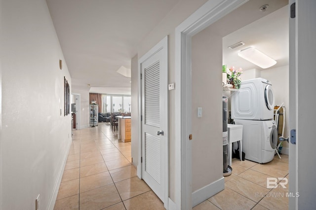 hallway featuring light tile patterned floors, visible vents, baseboards, and stacked washer and dryer