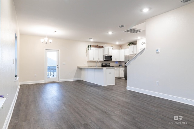 kitchen with kitchen peninsula, dark hardwood / wood-style floors, appliances with stainless steel finishes, a notable chandelier, and white cabinetry