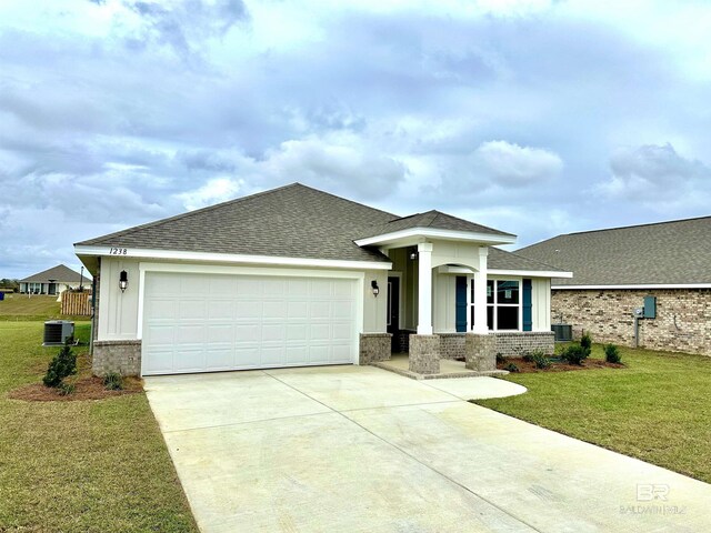 prairie-style home with a garage, central AC, a shingled roof, concrete driveway, and a front lawn