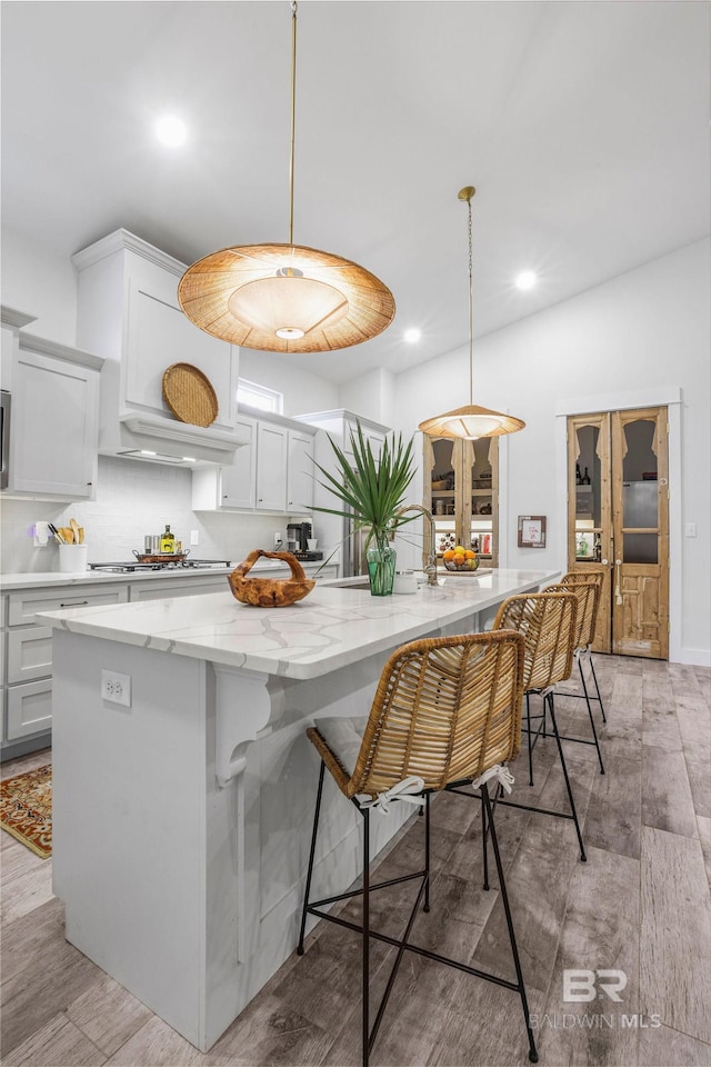 kitchen with stainless steel gas cooktop, white cabinetry, light wood-style floors, custom exhaust hood, and light stone countertops