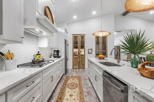 kitchen featuring light wood finished floors, custom exhaust hood, lofted ceiling, appliances with stainless steel finishes, and a sink